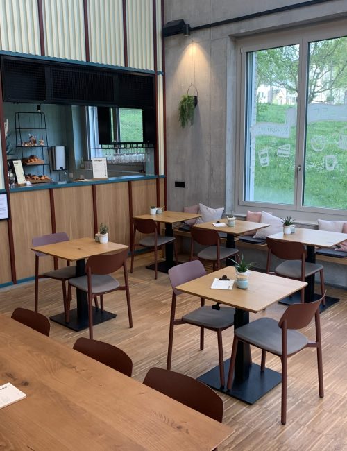 Café innen mit Holztischen Stühlen und Sitzbank sowie eine Vitrine mit Patisserie, Sandwiches und Backwaren