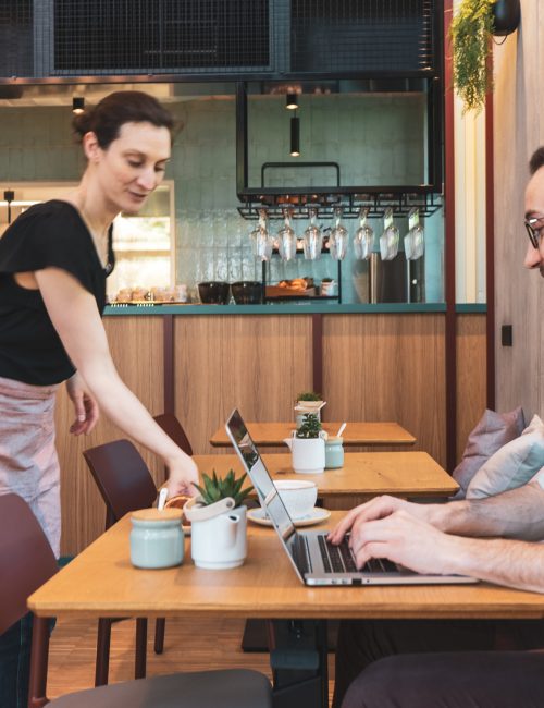 männlicher Gast welcher am Laptop arbeitet und gerade einen Cappuccino serviert bekommt