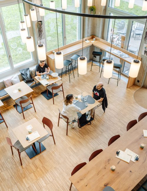 Café innen mit Holztischen Stühlen, Sitzbänken und einigen Gästen