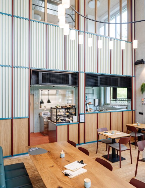 Café innen mit Holztischen Stühlen und Sitzbank sowie eine Vitrine gefüllt mit Patisserie, Sandwiches und Backwaren