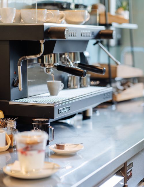 Siebträger-Kaffeemaschine mit welcher gerade ein Espresso gemacht wird und im Vordergrund ein Becher mit Joghurt, Früchten und Granola