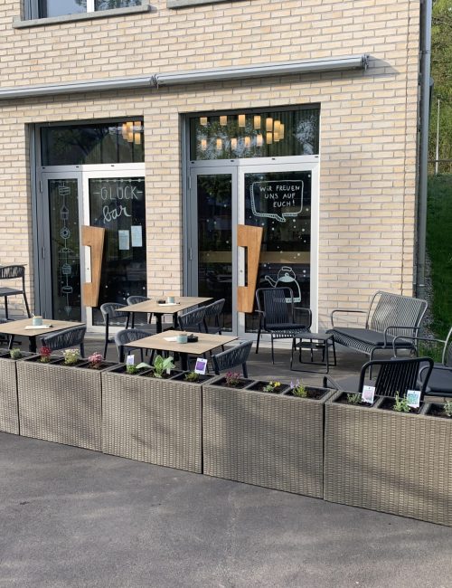 Terrasse mit Lounge, Tischen und Stühlen, welche mit bepflanzten Hochbeeten abgegrenzt ist